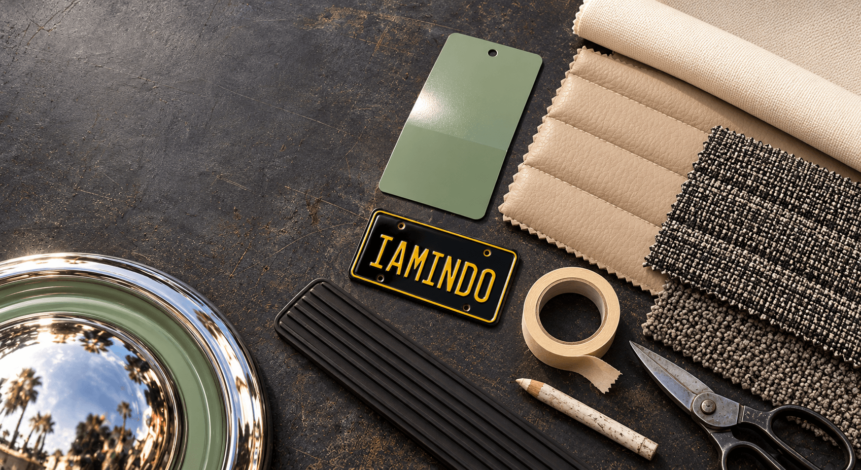 Finish samples on a dark workbench: a pistachio paint chip, beige vinyl, ivory canvas, salt-and-pepper weave, black rubber, a chrome dome cap and the IAMINDO plate